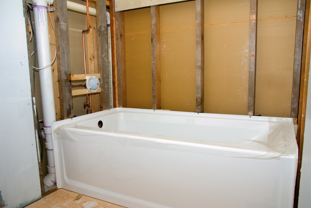 A bathroom with a bathtub in the foreground and a partially completed plumbing work on the wall in the background